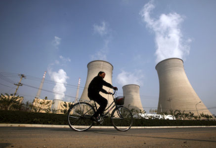 A woman rides her bicycle past the chimneys of a power station located on the outskirts of Beijing
