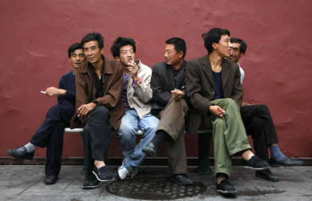 Migrant workers rest near a red wall beside the Tiananmen Square in Beijing
